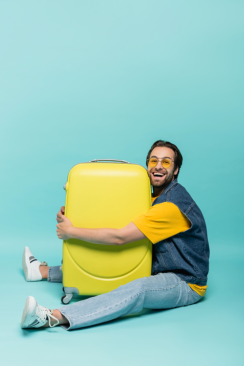 Cheerful man hugging suitcase on blue background