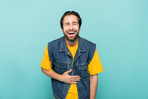 Excited man in denim vest laughing isolated on blue