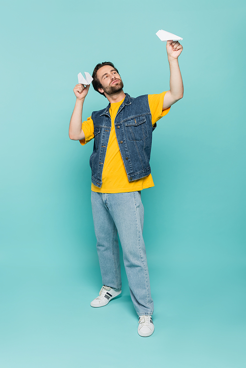 Full length of man playing with paper planes on blue background