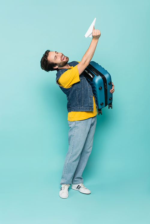 Laughing man holding suitcase and paper plane on blue background