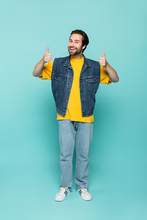 Smiling man in denim vest showing thumbs up on blue background