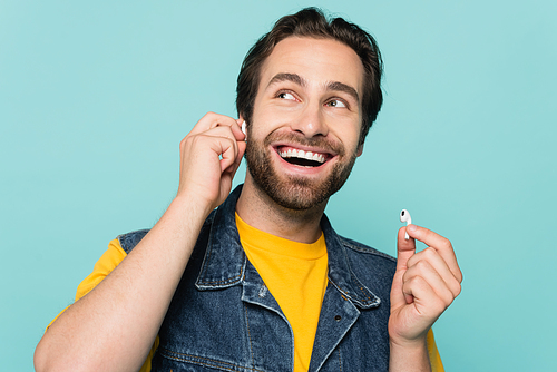 Smiling man holding earphones isolated on blue