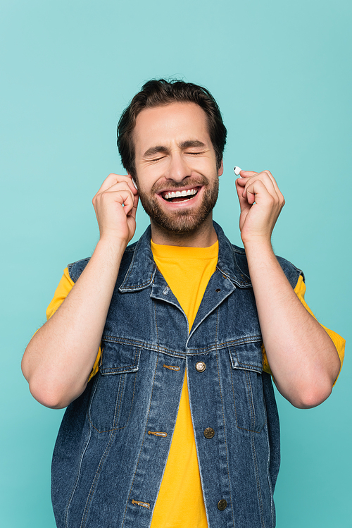 Cheerful man with closed eyes and earphones isolated on blue