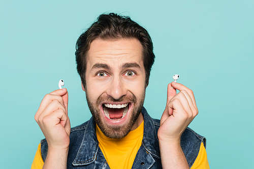 Excited man holding earphones and  isolated on blue