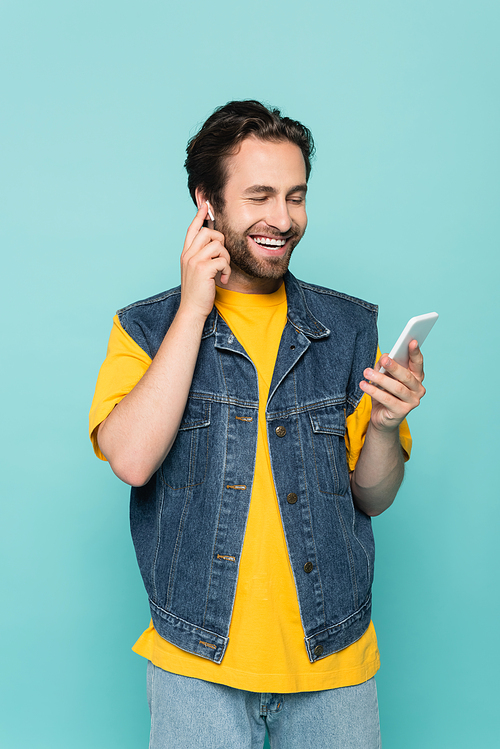 Smiling man in earphone using smartphone isolated on blue