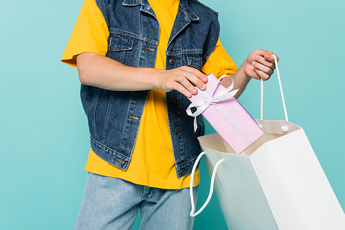 Cropped view of man putting gift box in shopping bag isolated on blue