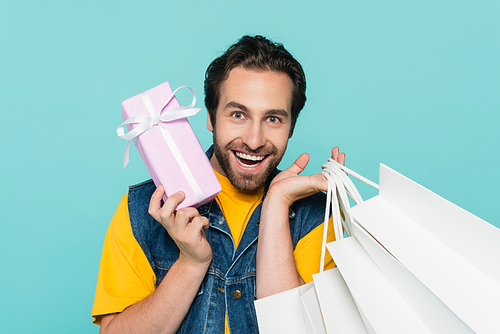 Cheerful man with gift and shopping bags  isolated on blue