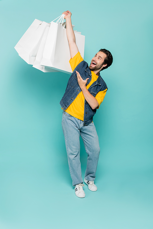 Excited man pointing at shopping bags on blue background