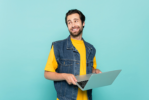 Smiling freelancer with laptop looking away isolated on blue