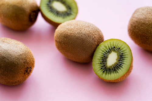 close up view of sweet whole and cut kiwi on pink