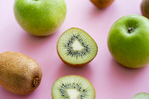 close up view of apples and sweet kiwi on pink