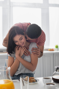 happy young couple hugging near table with breakfast, coffee and orange juice in kitchen