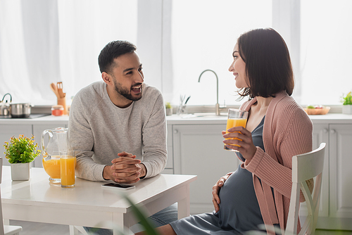 happy young man and pregnant woman sitting in kitchen