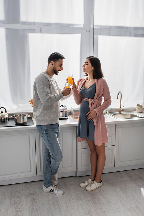 smiling young man standing near pregnant woman with orange juice in kitchen