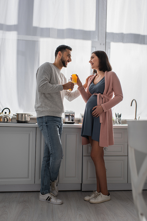happy young man and pregnant woman standing with orange juice in kitchen