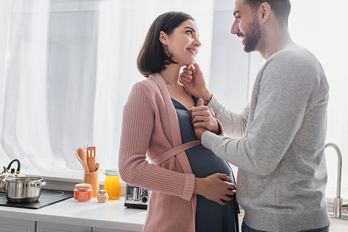 happy young man touching face of pregnant woman in kitchen