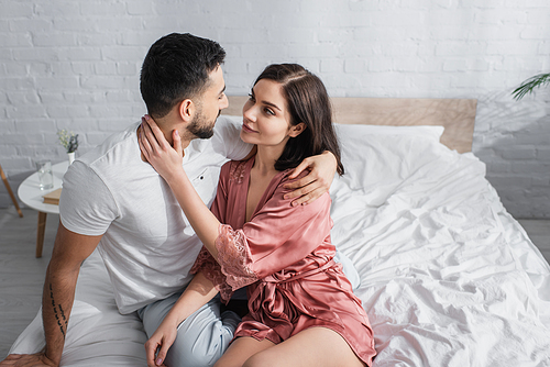 happy young couple gently hugging and looking at each other in bedroom