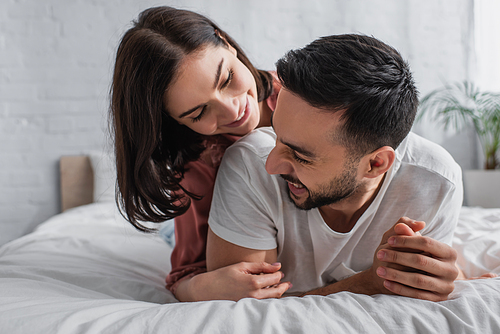 smiling young couple lying on bed with white linen and hugging in bedroom