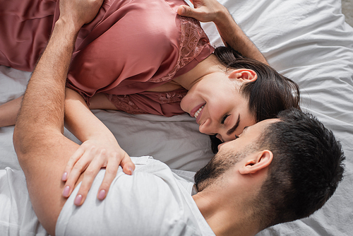 top view of young man lying on bed with white linen and gently hugging girlfriend in bedroom