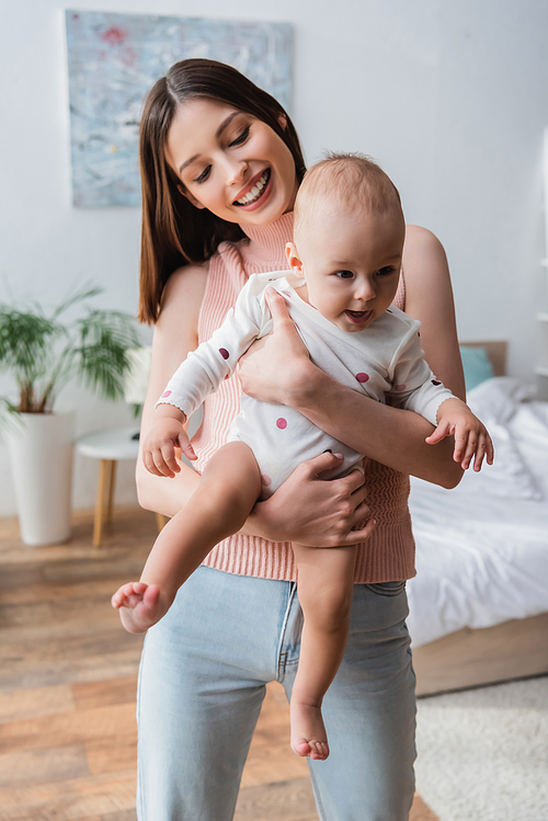 brunette smiling woman holding little kid in romper in bedroom