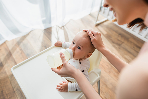 blurred woman touching head of baby boy while feeding him with milk