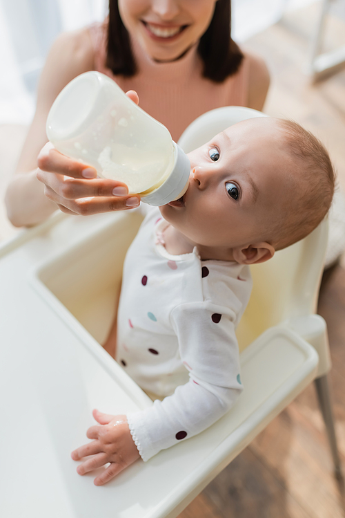 high angle view of little kid  while drinking milk from baby bottle in hand of blurred mom
