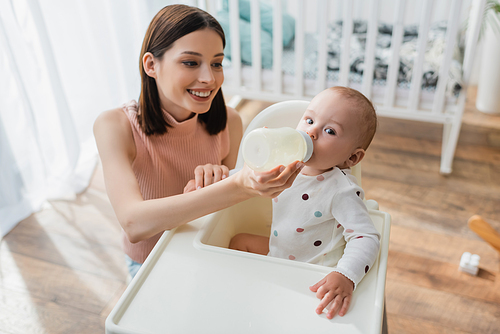 high angle view of happy brunette woman feeding son with milk at home