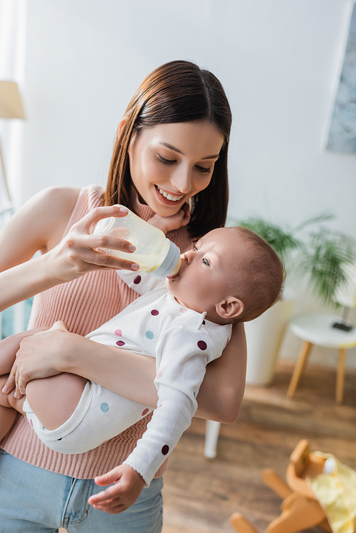 smiling brunette woman feeding toddler son with milk at home