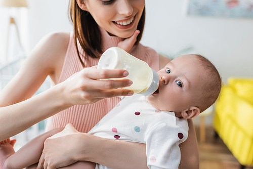 blurred woman smiling while feeding toddler son from baby bottle