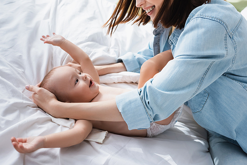 smiling woman embracing toddler son lying on bed at home