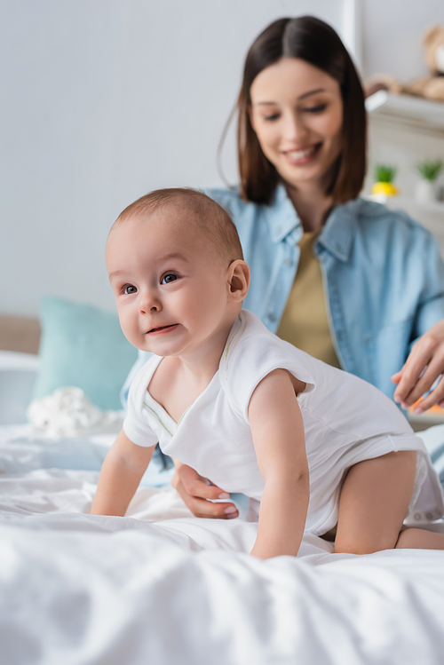 toddler boy in romper crawling on bed near blurred mother