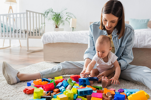 brunette woman with baby boy playing with building blocks on floor in bedroom