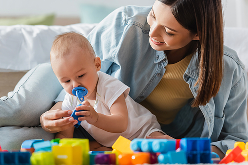 smiling woman with baby boy playing with blurred building blocks on floor