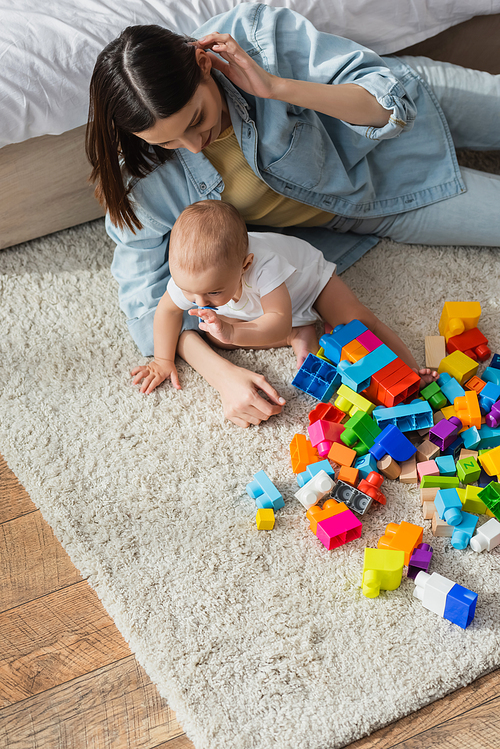 high angle view of brunette woman and her little son playing with building blocks on floor carpet