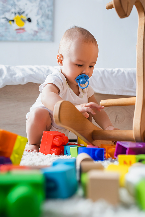 toddler kid with pacifier playing with blurred building blocks while sitting on floor