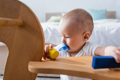 little boy with pacifier holding building blocks near blurred rocking horse