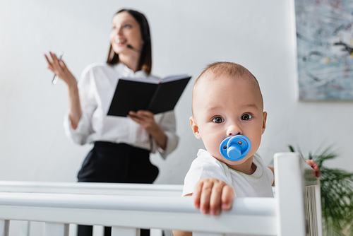 baby boy with pacifier  near blurred mother working at home