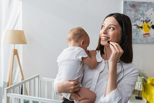 smiling woman in headset holding toddler son while working at home