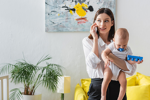 woman talking on cellphone while working at home with toddler kid in hands