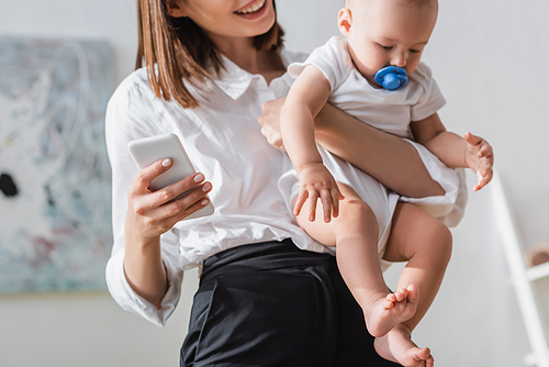 blurred woman holding smartphone and little son in romper