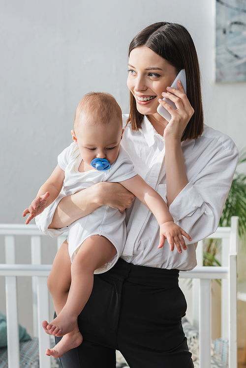 smiling woman talking on smartphone while holding baby boy in hands
