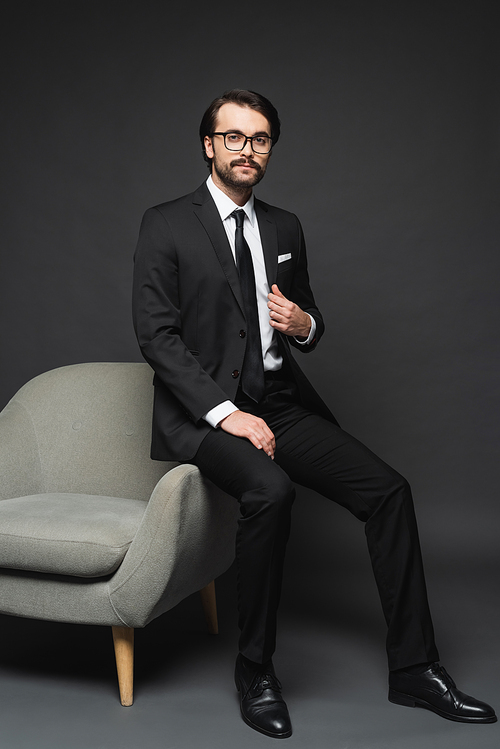 businessman in suit and glasses leaning on armchair on dark grey