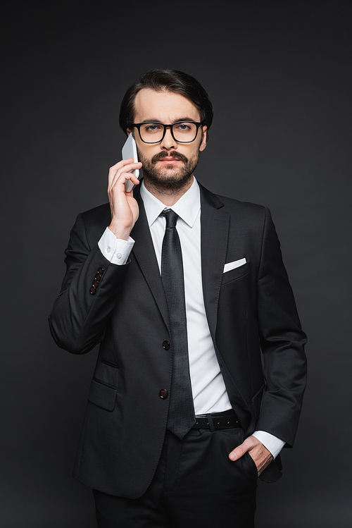 businessman in suit and glasses talking on smartphone on dark grey
