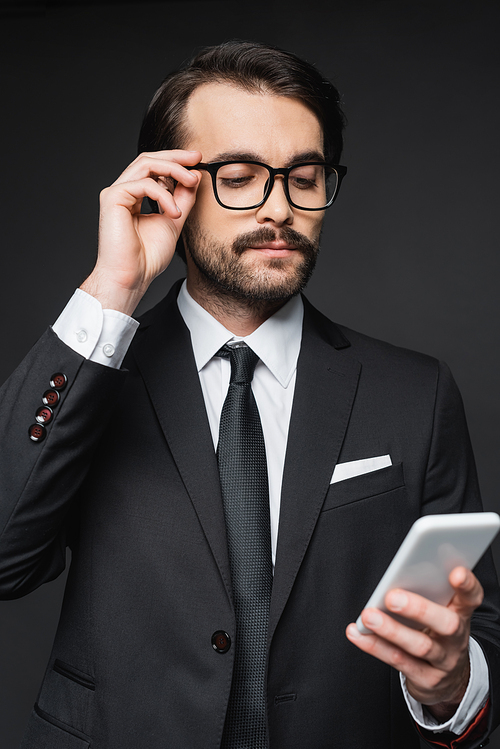 businessman in suit and glasses looking at smartphone on dark grey