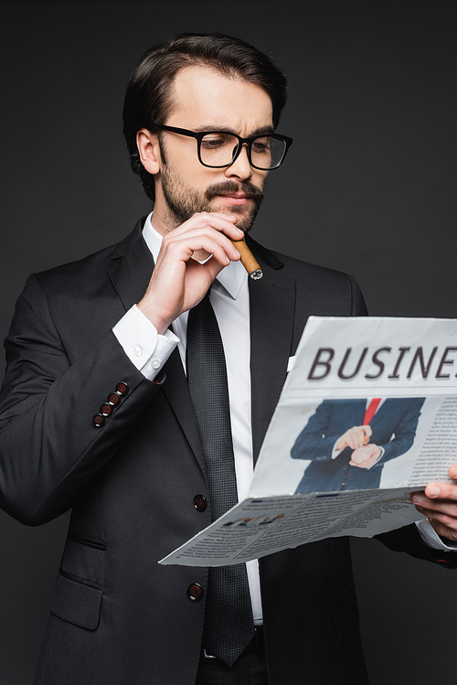 man in suit and glasses reading business newspaper and holding cigar on dark grey