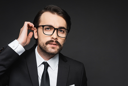 businessman with mustache in glasses adjusting hair on dark grey