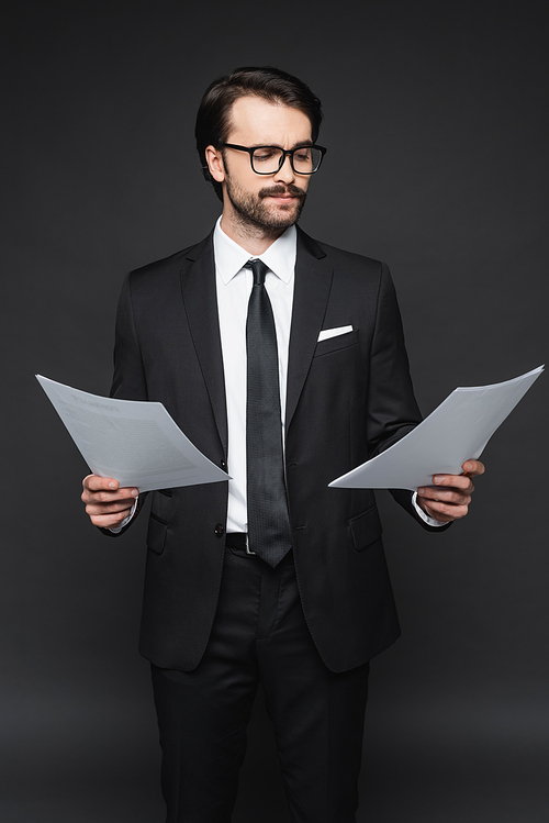 businessman with mustache in glasses looking at documents on dark grey