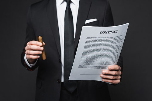 cropped view of businessman in suit holding cigar and contract on dark grey