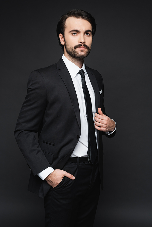 businessman with mustache  and posing with hand in pocket on dark grey