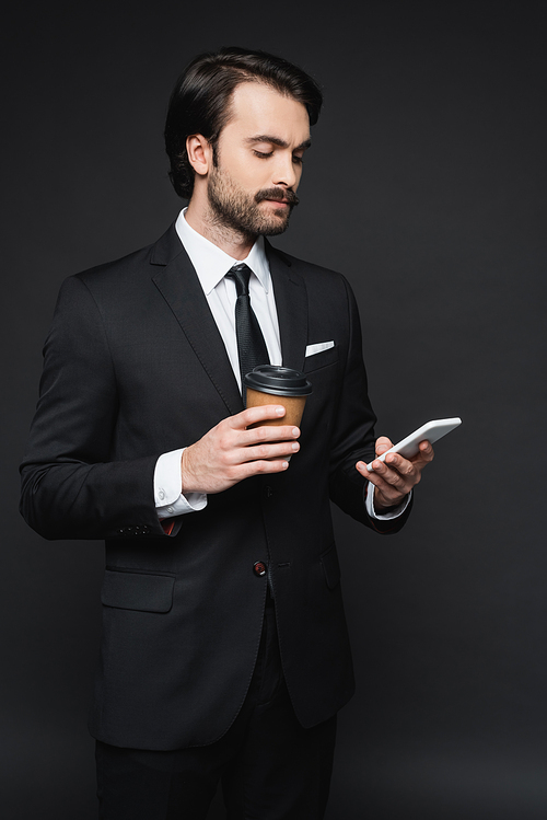 businessman with mustache holding paper cup and smartphone on dark grey
